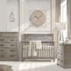 Baby nursery with white brick wall, big beige clock and sugarcane wooden 3 drawer dresser, 5 drawer dresser and crib