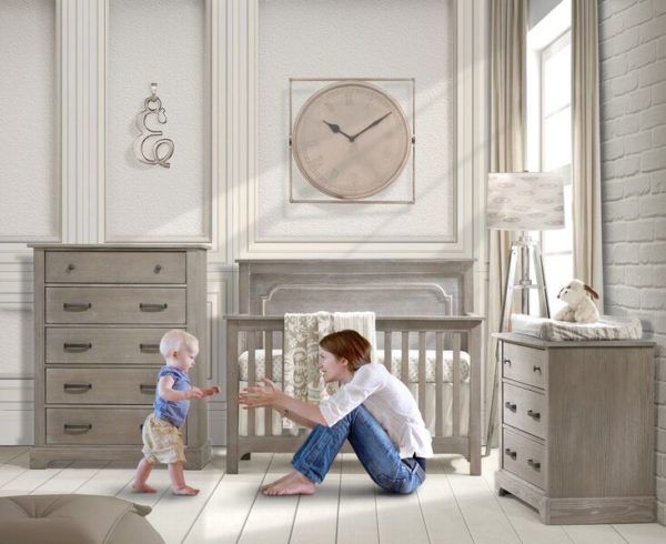 Baby nursery with white brick wall, big beige clock and sugarcane wooden 3 drawer dresser, 5 drawer dresser and crib with a mom reaching out to walking baby