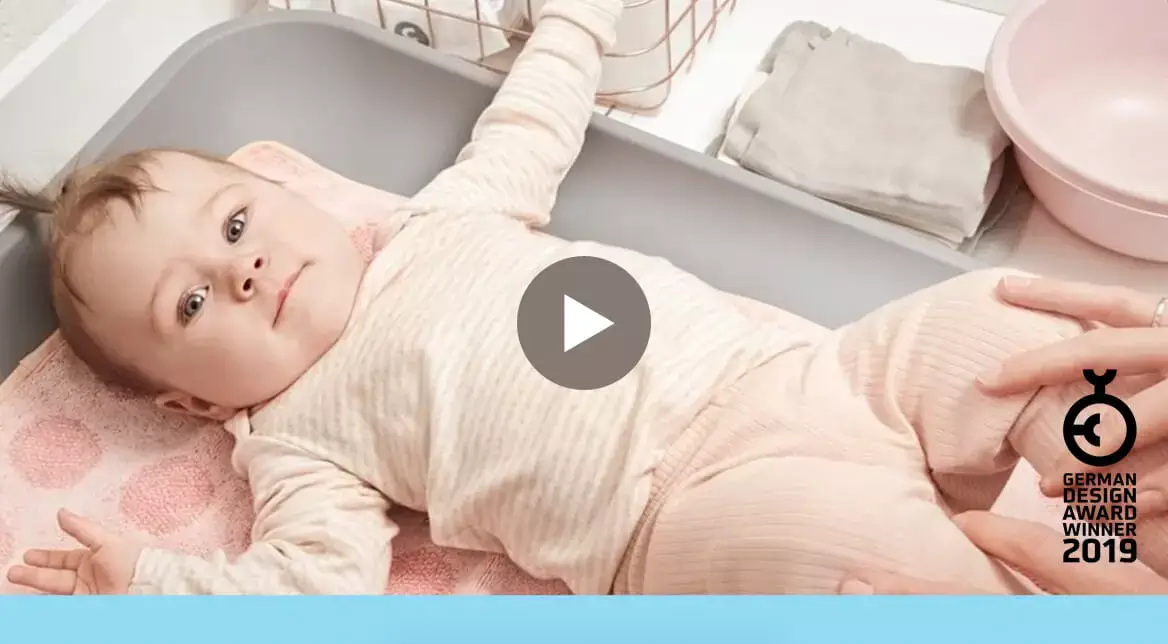 Baby in pink outfit laying on a grey changing mat
